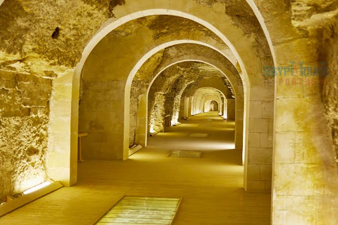 The illuminated underground gallery of the Serapeum of Saqqara showing arched stone ceilings and the passage between burial chambers